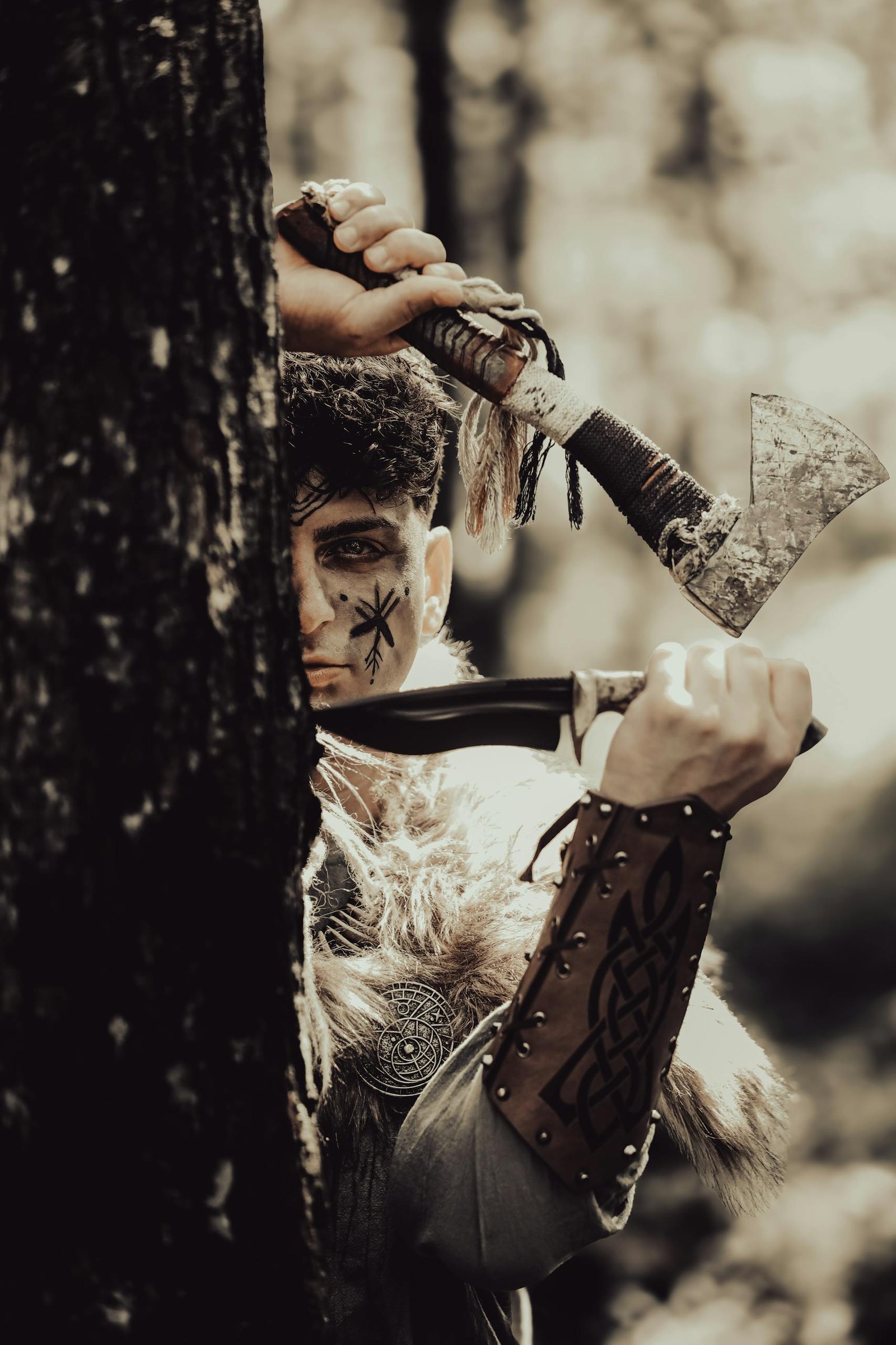 A fierce warrior in tribal attire with an axe and dagger, peering from behind a tree in the forest.