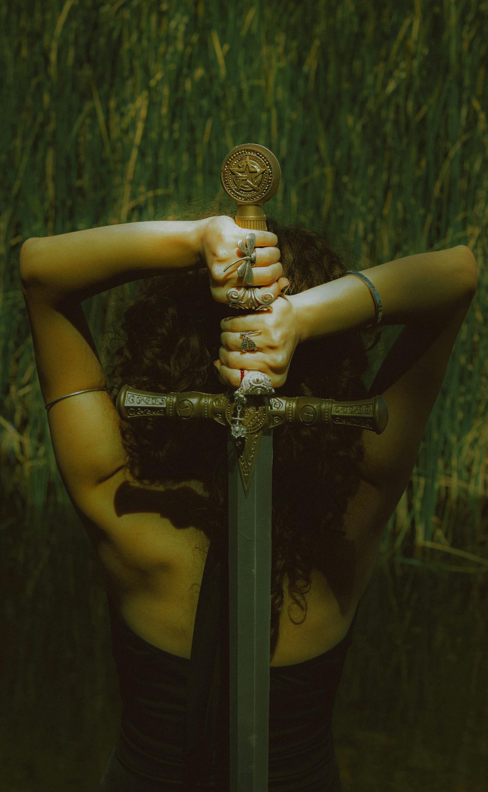 Back view of a strong woman holding a decorative sword, symbolizing empowerment and strength.