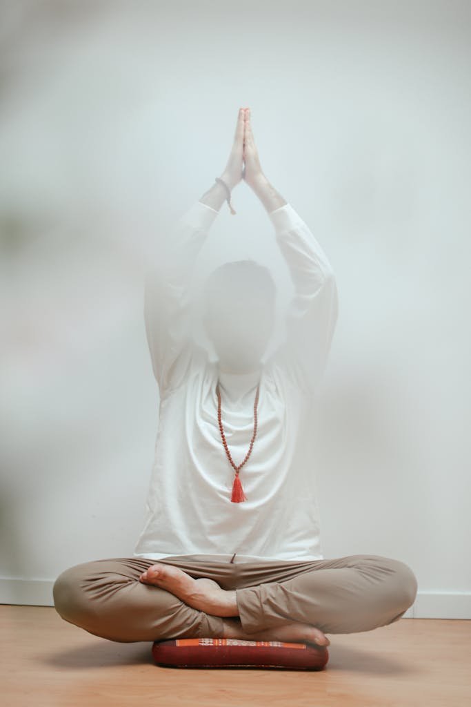 Person in lotus yoga pose practicing meditation indoors with soft focus.