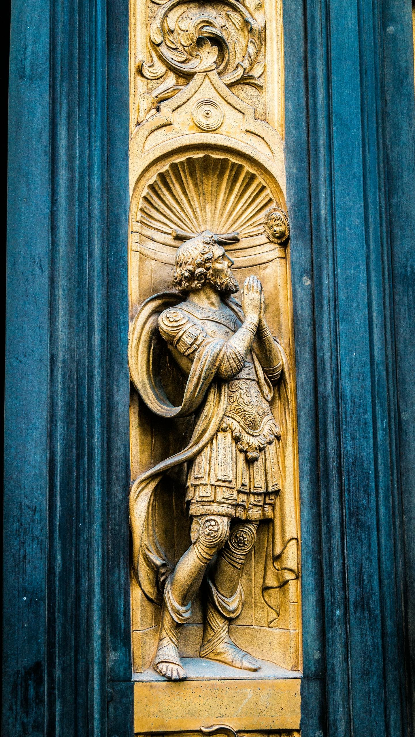 Shabby statue of praying man with clasped hands and ornaments decorating wall of medieval building