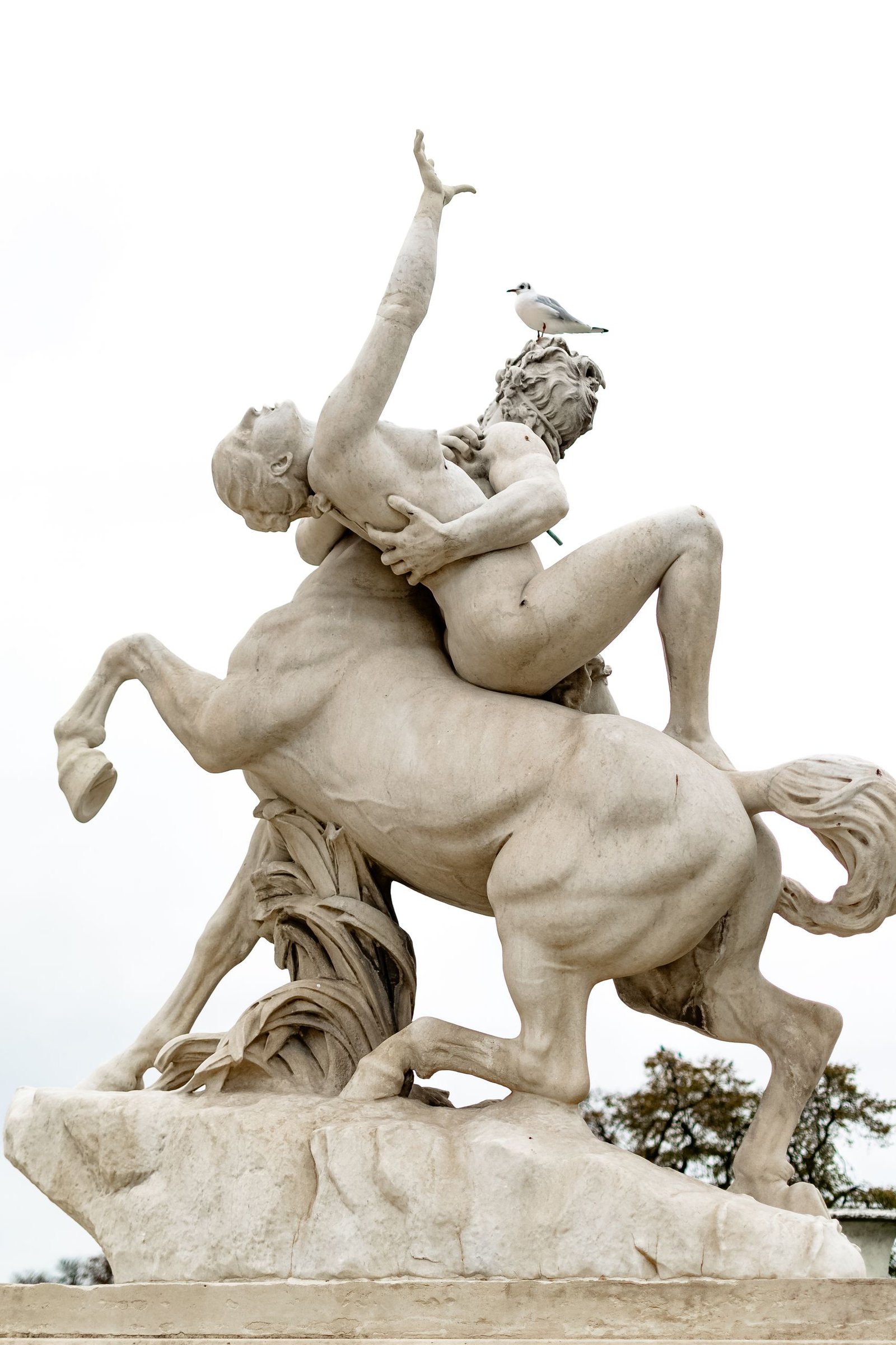A stunning stone sculpture featuring a centaur and male figure in Paris, topped by a bird.