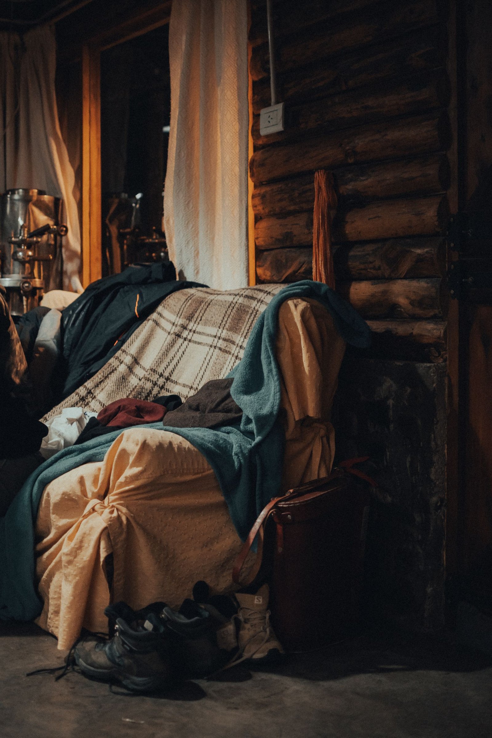 Warm and inviting log cabin interior featuring a cozy armchair draped with blankets and clothes in a rustic setting.